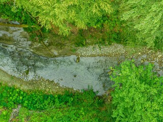 Aerial view of creek flowing through valley with dense forest. 
