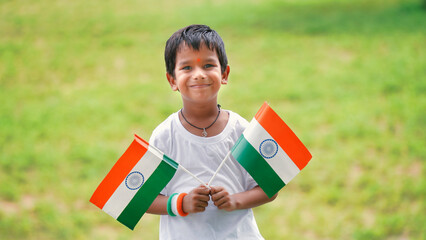 Handsome cute little Indian boy or kid in white ethnic wear standing infant of indian national flag...