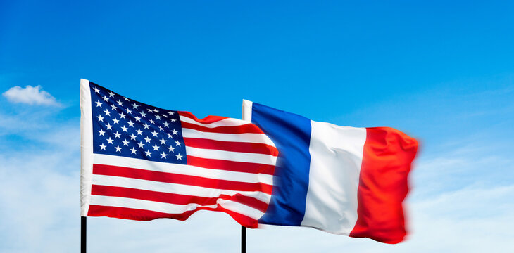 USA and France flags against blue sky background