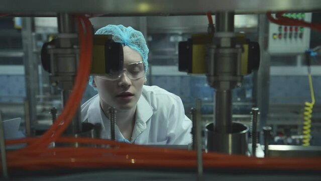 Female scientist in white coat and blue hat working in the control  machine of production line.