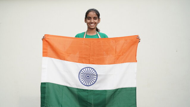 Cute Indian girl holding Indian flag in her hand and smiling. Celebrating Independence day or Republic day in India. A girl showing pride of Tiranga