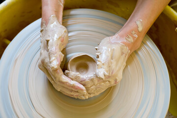 The hands of a potter sculpting a piece of clay on a rotating potter's wheel.