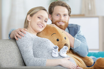 young happy couple expecting a baby on sofa with soft-toy