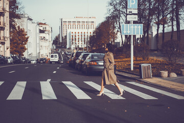 Young woman walks on the crossroad through the autumn city