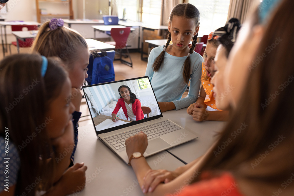 Wall mural Multiracial teacher and students video calling over laptop while studying online in classroom