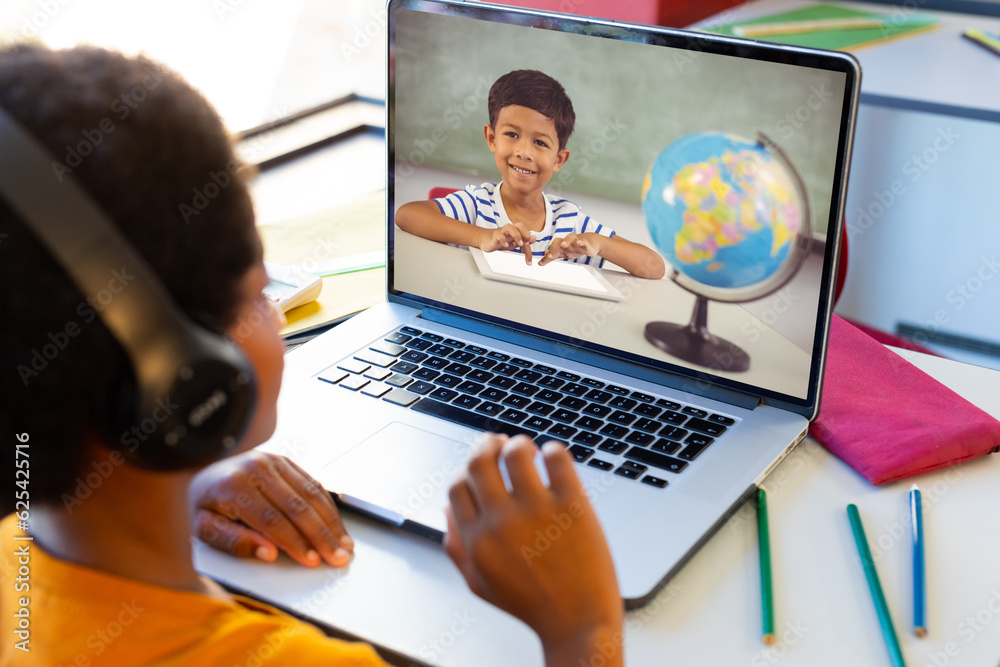 Canvas Prints Biracial boy wearing headphones and discussing with friend over video call on laptop at home