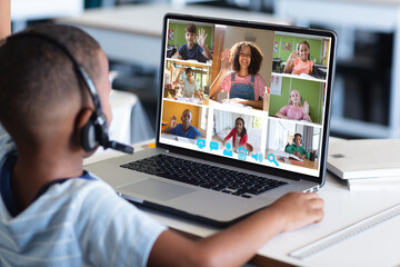 Fototapeta na wymiar African american boy looking at students and teacher waving hands over laptop during online class