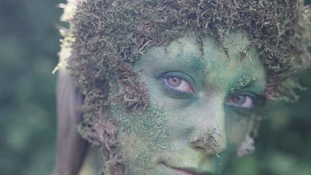 Close up of a female avatar wearing green bodypaint looking towards the camera in a forest, in the style of nature-inspired forms