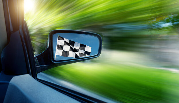 Car driving fast with checkered race flag in rear view mirror