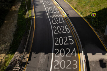 The years from 2023 to 2029 are written on the road with a turn to the left, the road goes in the...