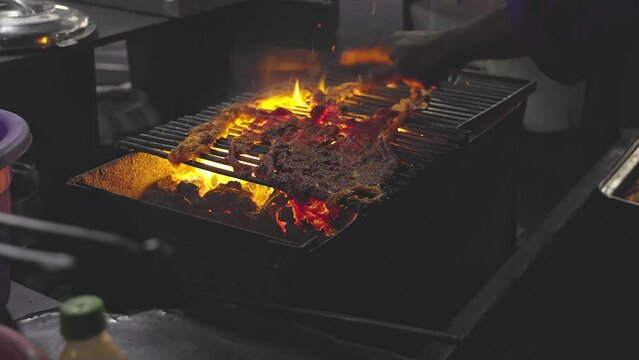 Closeup of a man grilling marinated raw meat or beef slices on a charcoal grill