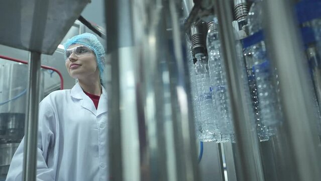 Female quality control worker inspecting water bottle on production line in drinking water factory