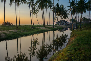 Sunrise over the beautiful beach with full of coconut trees and a small hut with reflection 