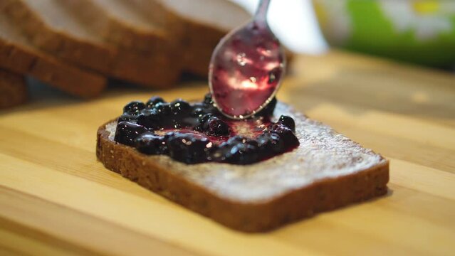 Spreading jam on rye bread with butter. Delicious and healthy breakfast. Sandwich with butter and jam. Close-up.