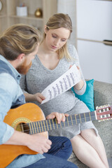 man playing guitar beside his pregnant wife