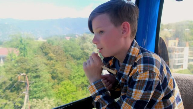 Interested teen boy tourist sitting in funicular cabin of cable car in Batumi Georgia. Teenager on vacations travelling in mountains admiring breathtaking views. Travel, tourism, journey, wanderlust.