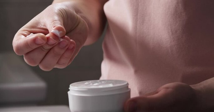 Woman with jar smearing skin cream on fingers to feel it texture indoors, closeup