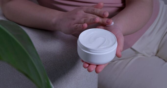 Woman with jar applying skin cream indoors, closeup