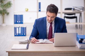 Obraz premium Young male employee reading book at workplace