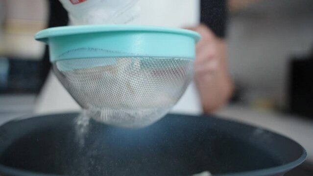 A woman is pouring flour into a sieve to sift it, in slow motion.