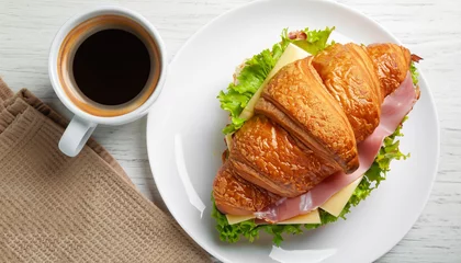 Photo sur Plexiglas Boulangerie Fresh croissant sandwich with ham, cheese and salad leaf with coffee on white table, top view