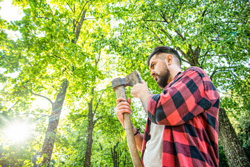 Lumberjack man. Chopping wood. Brutal lumberjack bearded man in woods on a background of trees....