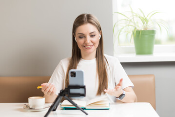 A freelancer girl records a video blog on a mobile phone in a cafe. Freelance concept.
