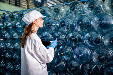 Female Caucasian scientist worker checking the quality of bottles in the warehouse at the industrial factory. Worker holding clipboard tablet.