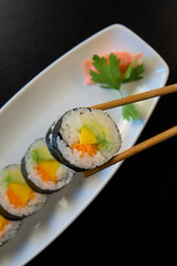 Wholesome Sushi Delight: Top-View of Hand Enjoying Vegetable-Filled Futomaki Sushi with Chopsticks - Healthy Alternative Cuisine with Copyspace