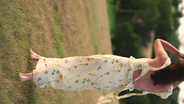 A young lady walks barefoot in a field at sunset. A girl in a beautiful yellow dress poses at sunset in a field. 4K video of a woman in nature.