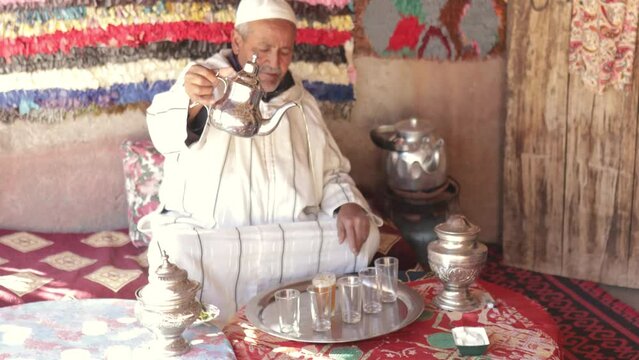 Moroccan senior man in traditional dress serving mint tea on outdoor terrace