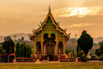 The background of the setting sun around the mountain range and there is an old church at Chiang Rai Province of Thailand or Wat Huai Khian, with beautiful old sculptures.