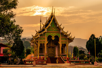 The background of the setting sun around the mountain range and there is an old church at Chiang Rai Province of Thailand or Wat Huai Khian, with beautiful old sculptures.
