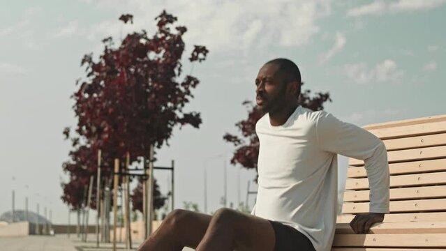 Tilt up shot of young black man doing triceps dips exercise by street bench outdoors in city during morning workout