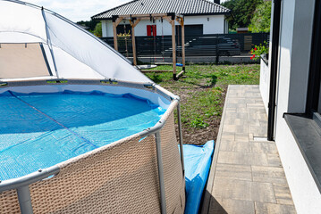 A large expansion pool with a diameter of 3.96 m, set in the yard next to the house, covered with a solar mat.