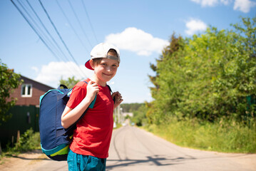 a boy with a big sports bag came for summer holidays in the village, countryside. portrait of a happy child on the road, village street in summer