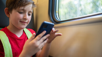 smiling boy 10 years old plays in a mobile, sits by the window in a suburban electric train in summer