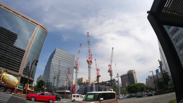 Lots of cranes lifting construction materials in urban area. Construction site of huge building. Construction industry. Car moves across the street
