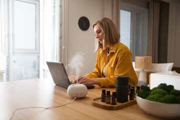woman working on laptop from home near essential oil aroma diffuser humidifier diffusing water...
