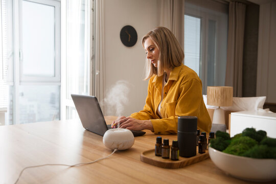 woman working on laptop from home near essential oil aroma diffuser humidifier diffusing water articles in the air. Aroma therapy