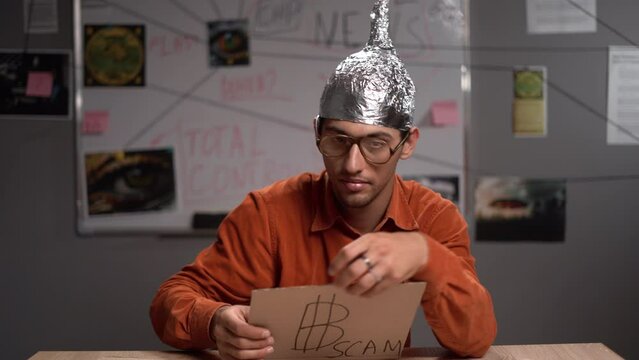 Male conspiracy theorist in a protective foil cap and glasses debunks myths. Conceptual cryptocurrency bitcoin with the word Scam