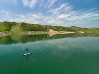 A bearded man swims on a SUP board on a lake among the rocks. Stand Up Paddling. Mountain lake with azure water