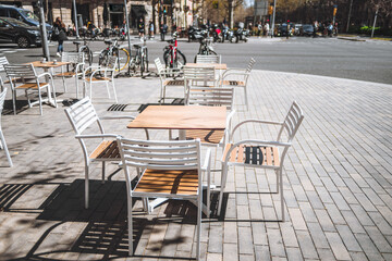 Barcelona; Ample sidewalk space adorned with empty, inviting white and brown tables and chairs, perfectly spaced for visitors to savor moments while bicycles rest nearby, a captivating spot to unwind