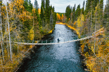 Aerial view of autumn fall leaf color in the woods and blue river with suspension bridge with...