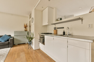 a kitchen and living room in an apartment with white cabinets, wood flooring and grey sofas on the right side