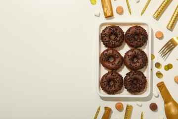 Chocolate donuts on plate and party supplies on white background, space for text