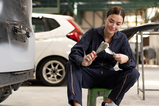 Woman auto mechanic putty damaged car body. Female repair technician prepare for painting crash vehicle body from accident by leveling out before applying primer. Empower women in automobile industry.