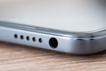 Macro shot of upper panel of mobile phone with speaker and jack port for headphones. Close up of grey modern phone on the table