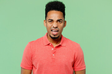 Young dissatisfied displeased disappointed sad man of African American ethnicity wears pink t-shirt looking camera isolated on plain pastel light green background studio portrait. Lifestyle concept.