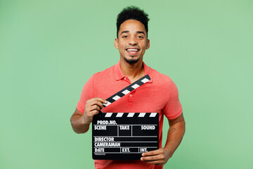 Young fun man of African American ethnicity he wear pink t-shirt hold in hand classic black film making clapperboard isolated on plain pastel light green background studio portrait. Lifestyle concept. - obrazy, fototapety, plakaty